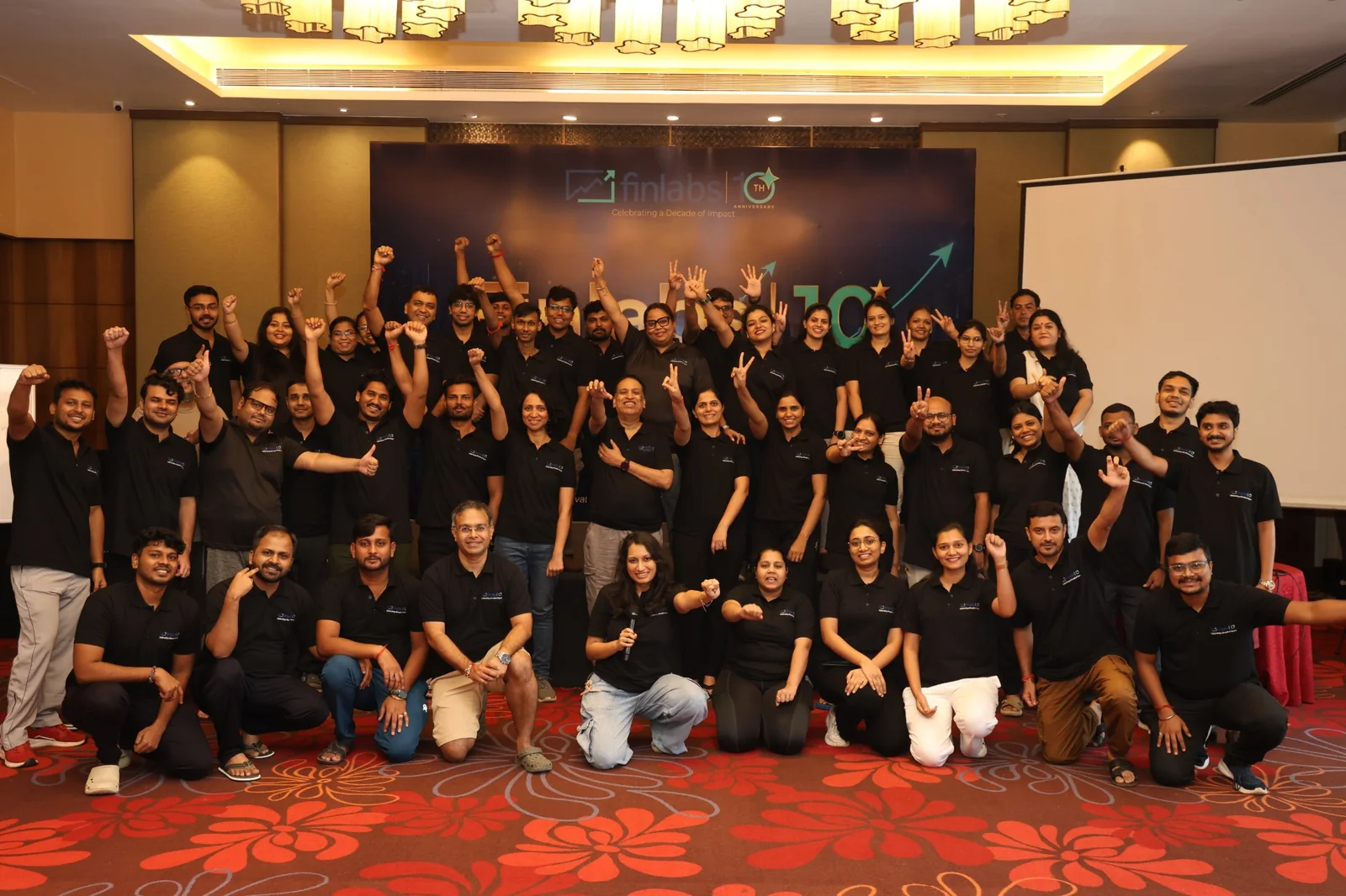 The Finlabs team in matching black polo shirts, celebrating the company’s 10th anniversary in front of the anniversary banner
